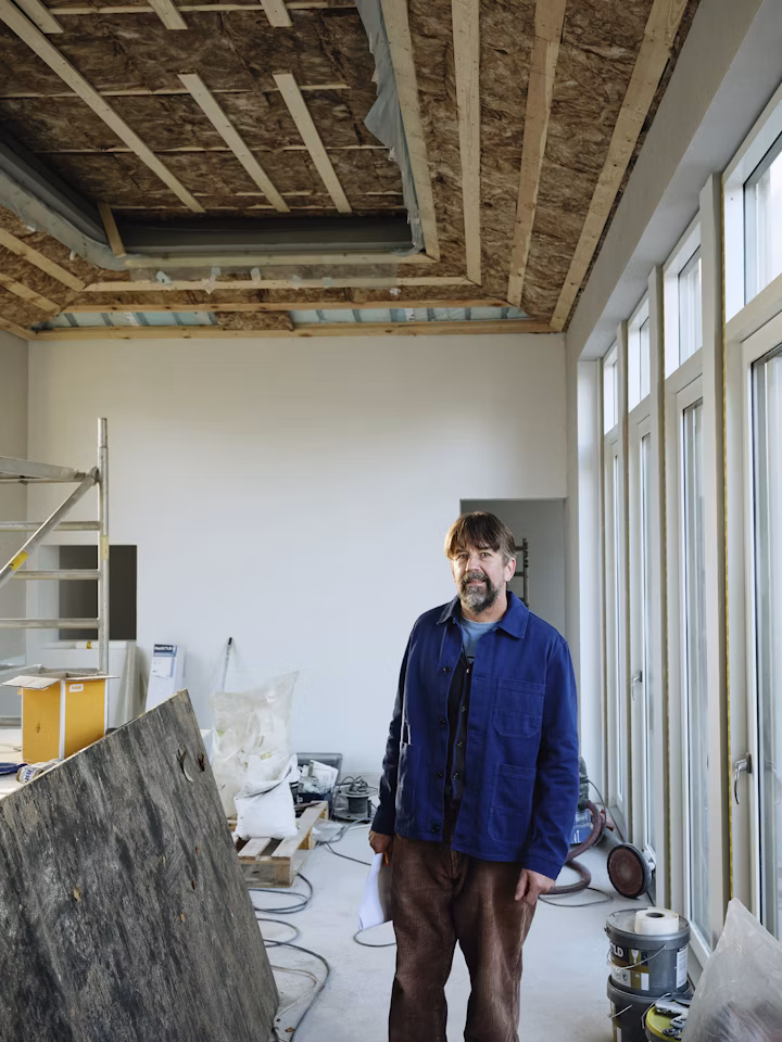 Mike Sullivan standing in a partially finished residential interior, exposed ceiling framing above and natural daylight from a wall of windows.